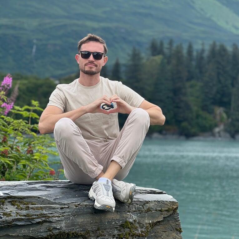 Photo of SBS employee sitting on a rock making a heart shape with his hands over his heart